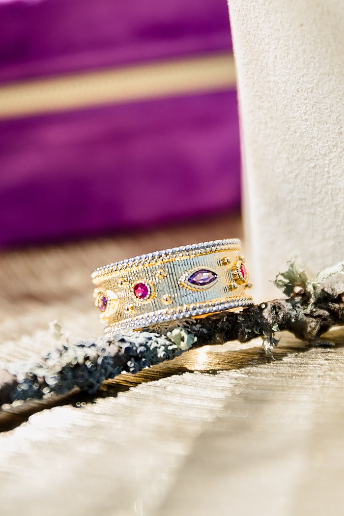 Gold statement ring with multicolor baguette stones displayed on textured surface