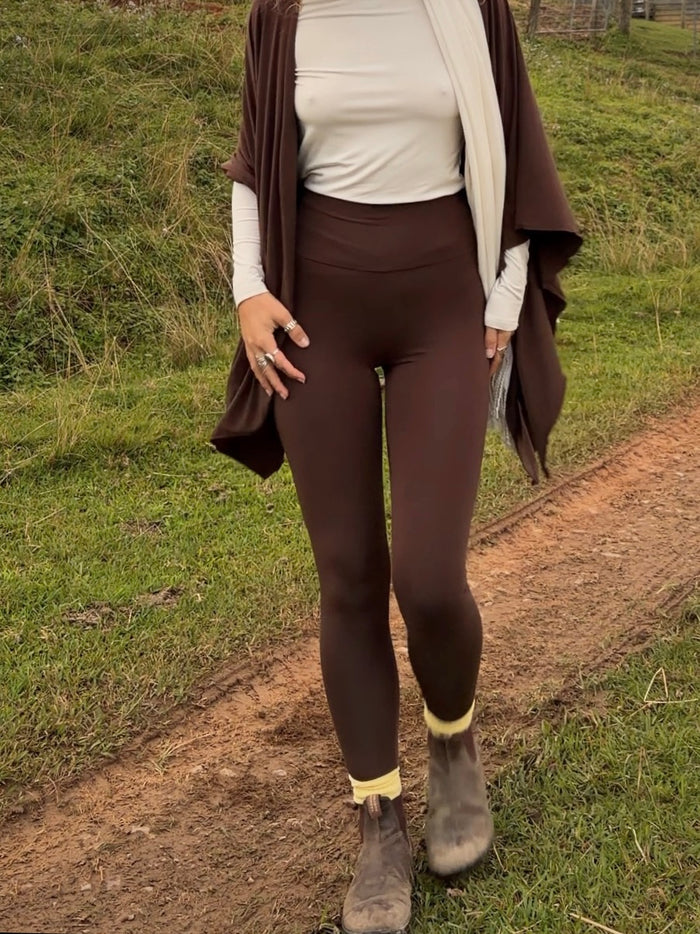 Person wearing brown leggings and a cardigan standing on a grassy path.