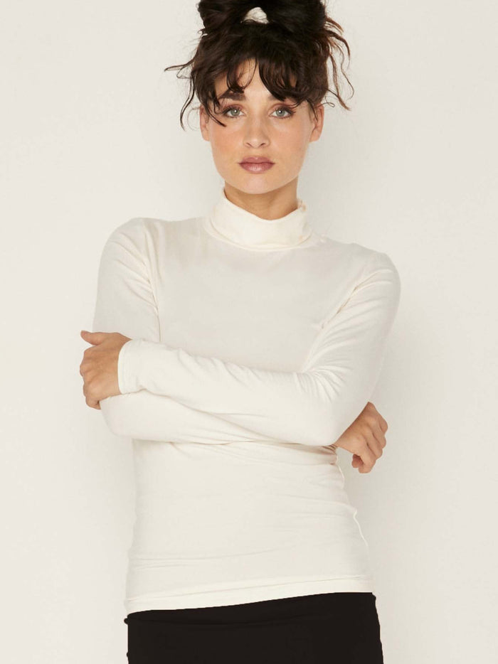 Model wearing cream high roll neck fitted skivvy, fitted long sleeves, women's bamboo clothing