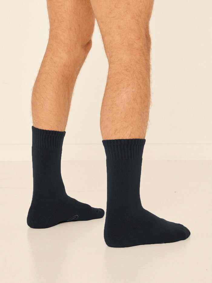 Model wearing black mid rise thick work, hiking, bed socks with ribbed top and thick cushioned sole, bamboo socks
