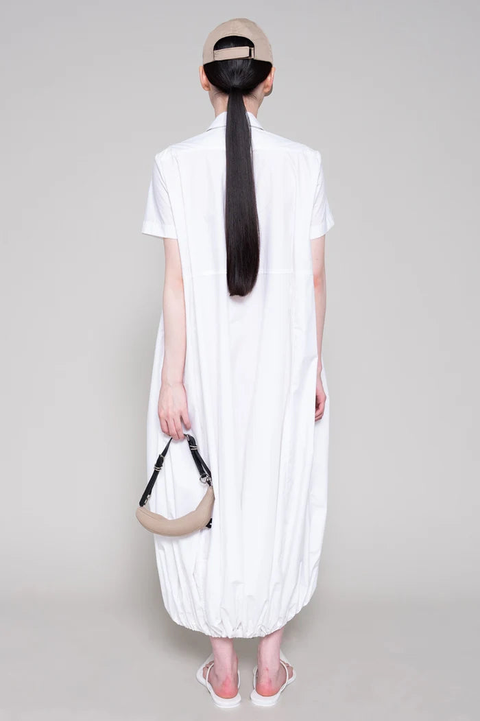 Person wearing a white dress with beige cap and bag on plain background