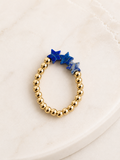 Betsy Stretch Gemstone Ring featuring natural blue gemstone beads and gold-plated stainless steel beads displayed on a marble surface.