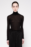 A model wearing a black sheer long-sleeve turtleneck top and black trousers, photographed against a plain light gray studio background.