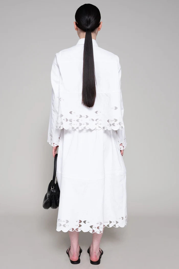 Person wearing a white shirt and skirt with cut-out details on a plain background