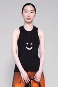 Person wearing a black sleeveless top with a smiley face design on a plain background