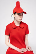 A model wearing a matching red pleated cap and short-sleeve polo dress, posed against a light gray studio background.