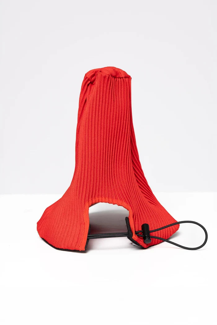 A red baseball cap with the head portion made of a pleated fabric which points upwards.