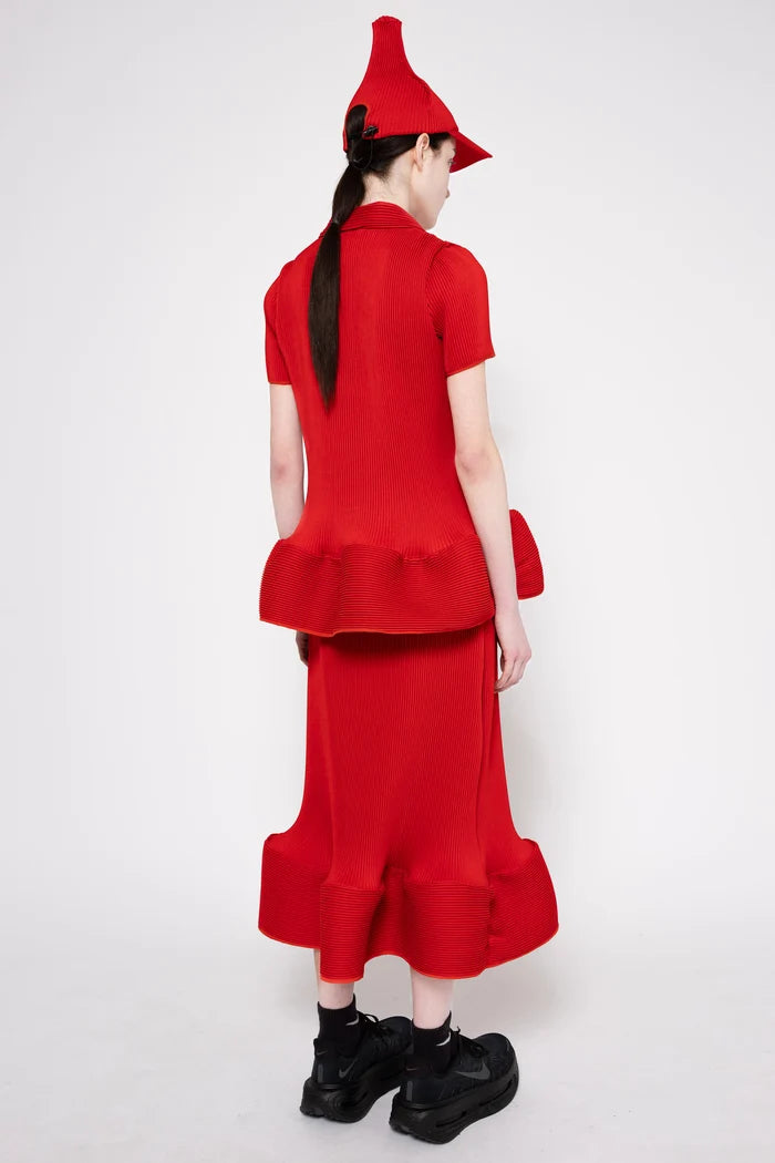 A model shown from the back wearing a bright red two-piece outfit consisting of a short-sleeve top with a ruffled hem and a matching long skirt, along with a pointed red hat and black shoes, against a plain light gray background.