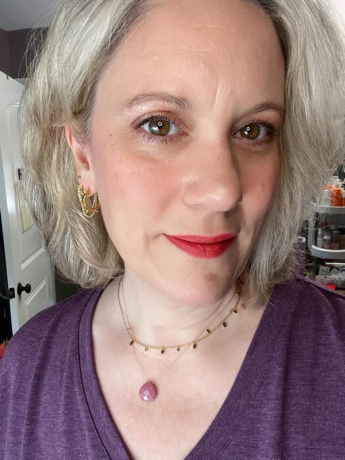 Model wearing VEITA Jewelry layered gold necklaces with disc charm chain and pink gemstone pendant, plus gold textured hoop earrings