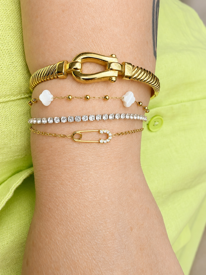 Model wearing the Kate Layering Bracelet which is second down from the top layered with coordinating gold bracelets, featuring delicate mother of pearl accents and an 18kt gold-plated stainless steel chain.