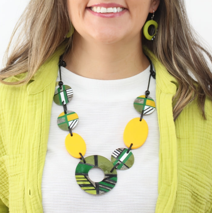 Woman wearing a colorful necklace with a white shirt and green jacket.