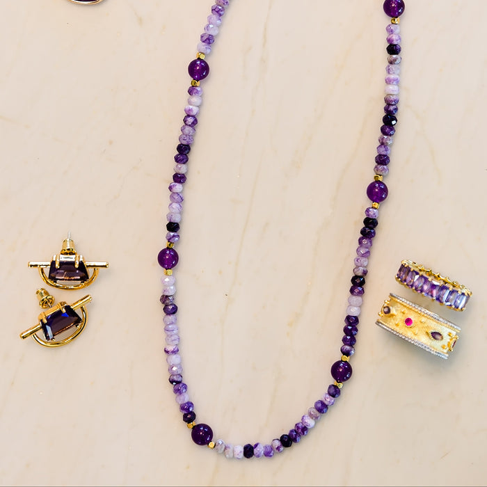Purple beaded necklace and earrings on a beige background