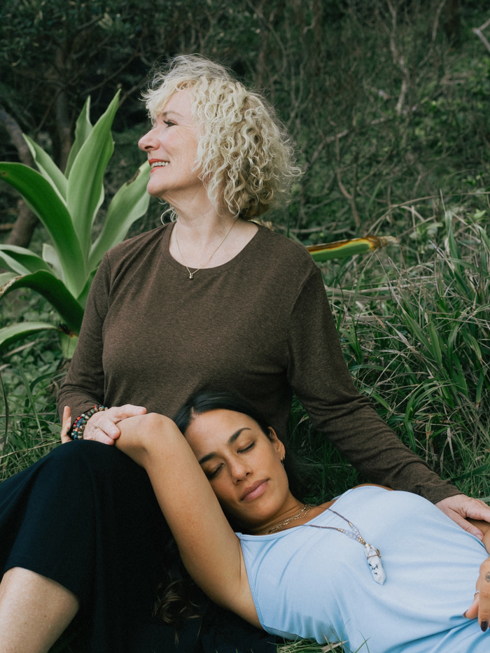 Two women sitting together in a natural setting with greenery.