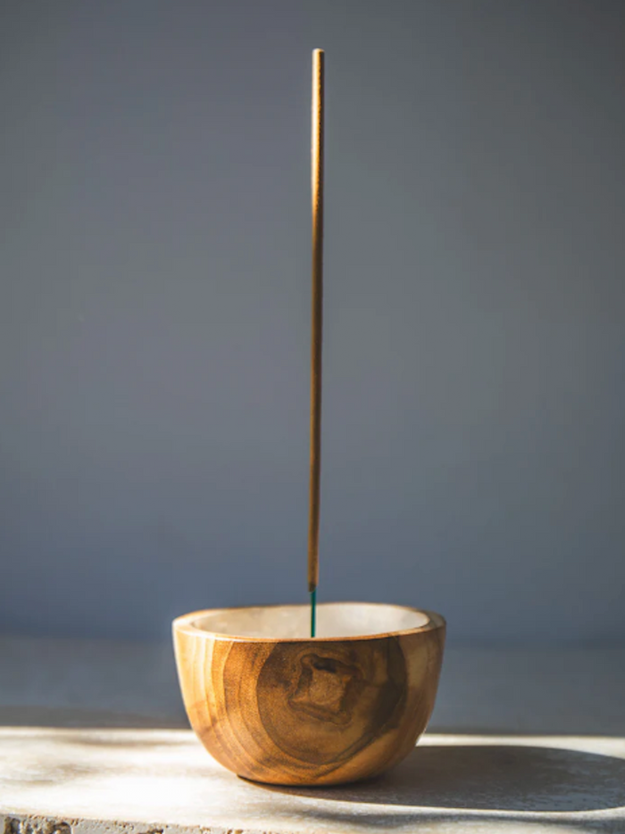 Shell lined wooden incense bowl with a single incense stick on a grey background