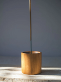 Wooden cylindrical incense holder with a single stick of incense on a grey background