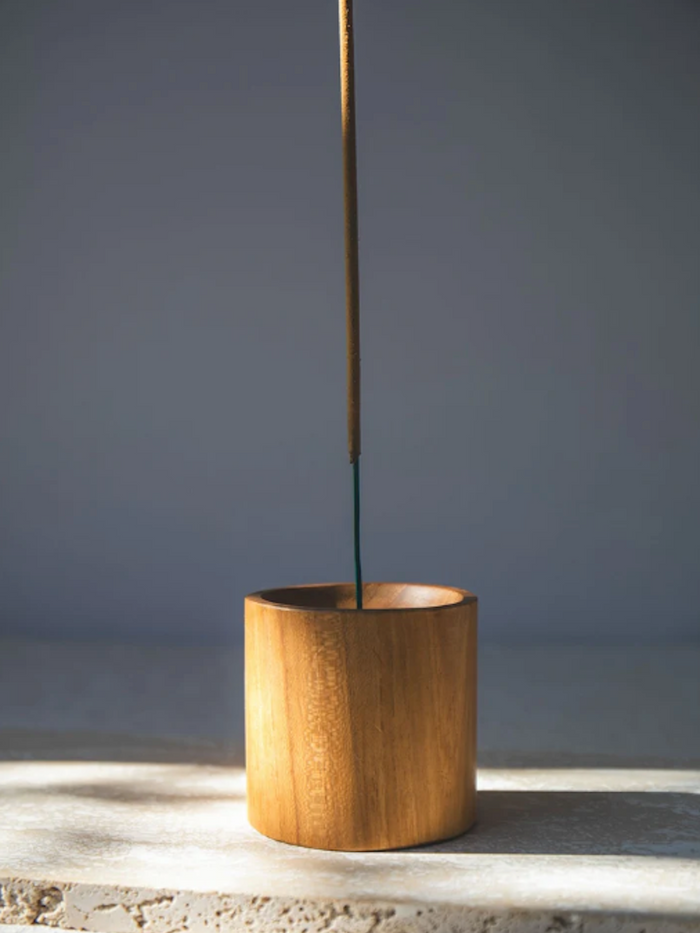 Wooden cylindrical incense holder with a single stick of incense on a grey background