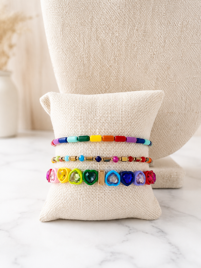 Love is Love Bracelet stacked with Prism Bracelet and Iris Bracelet, colorful beaded bracelets on a linen jewelry pillow