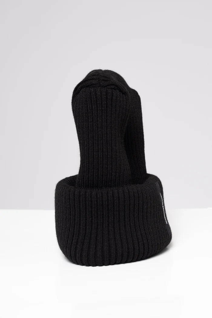 A black ribbed knit beanie hat with a folded cuff, featuring a small black vertical label on the side with white text that reads 'MELITTA BAUMEISTER'. The hat is photographed on a clean, light gray studio background.