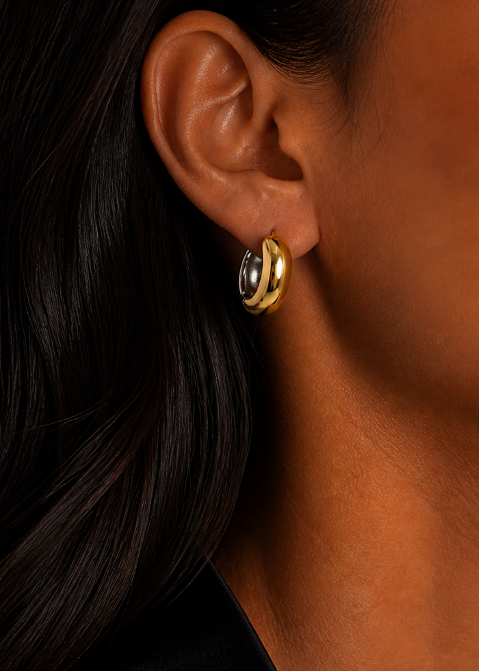 Close-up of an ear wearing a gold hoop earring with a black background