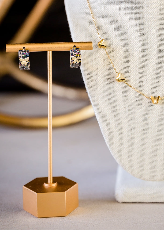 Gold necklace on a mannequin bust with earrings on a stand in the background.