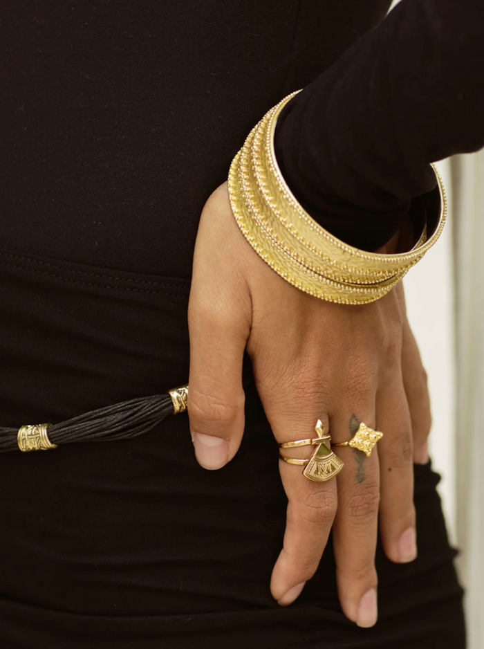 Close-up of a hand wearing gold brass bangles and rings on a black background