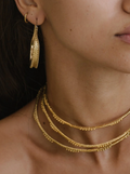 Close-up of a person wearing brass gold hoop earrings and necklaces.