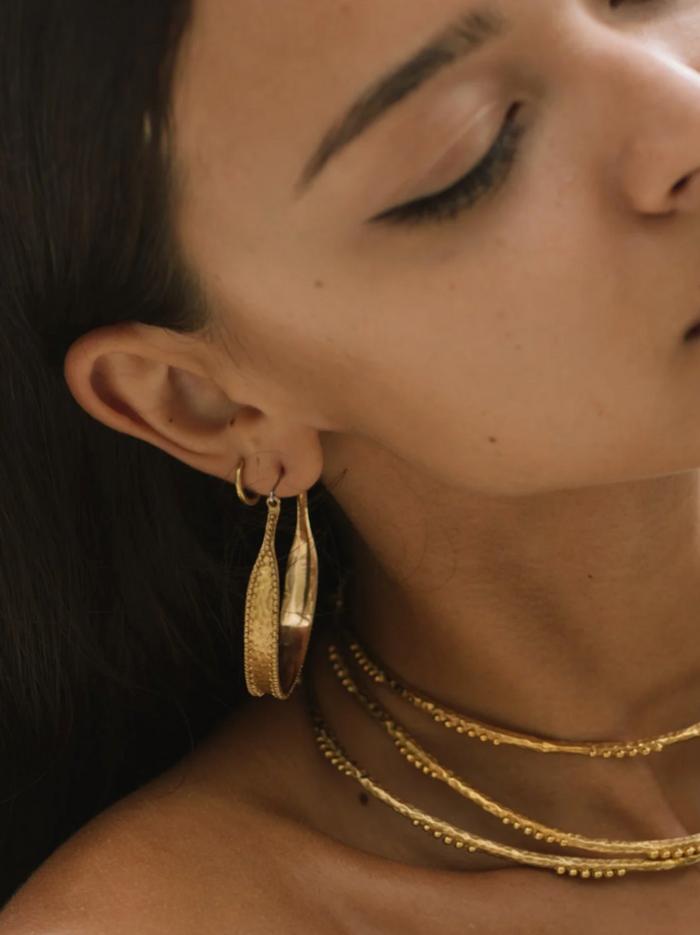 Close-up of a person wearing gold hoop earrings and necklaces.