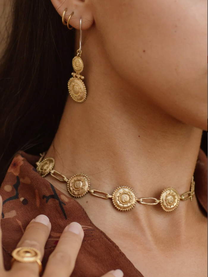 Close-up of a person wearing gold earrings and a matching necklace.
