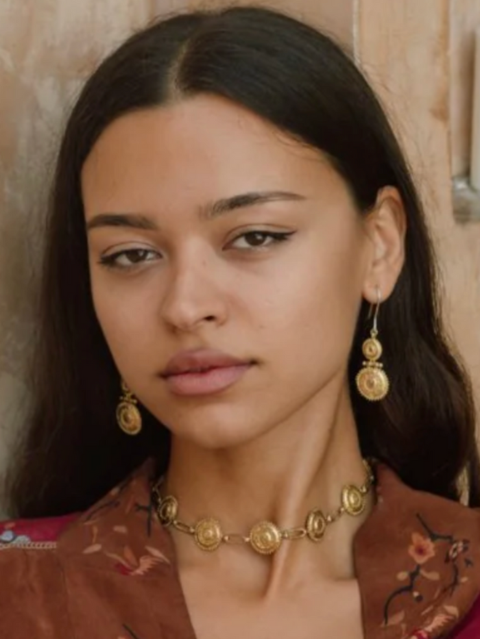 Woman wearing gold earrings and a necklace with a neutral background