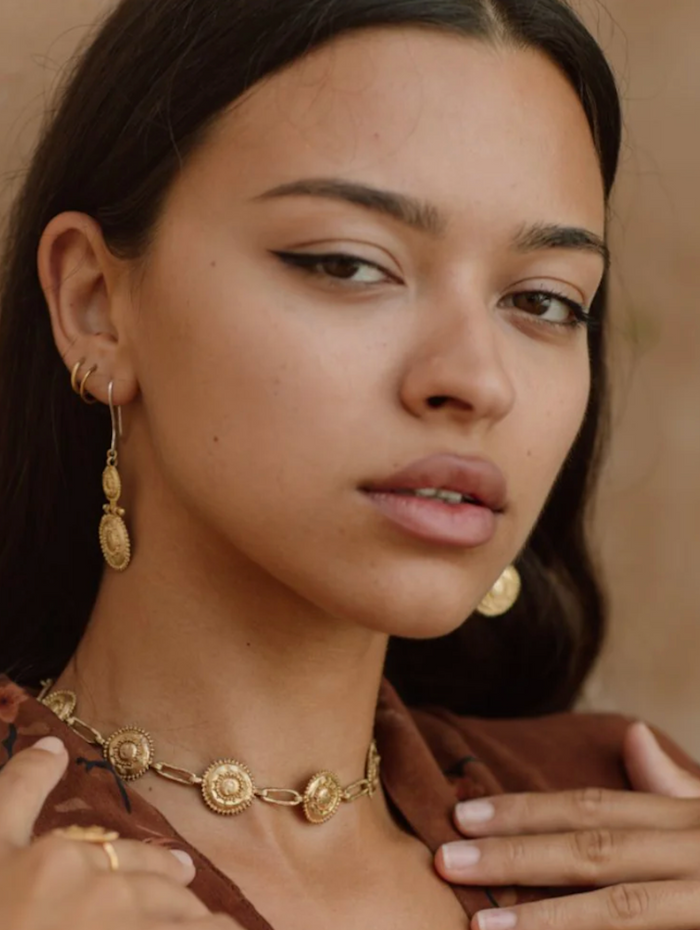 Close-up of a woman wearing gold jewelry against a neutral background