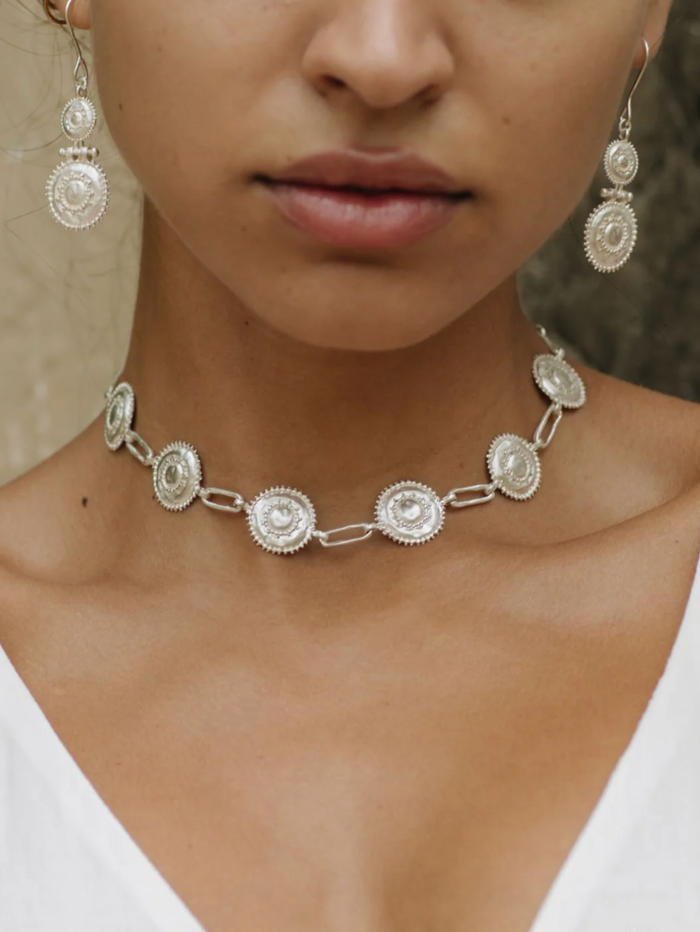 Close-up of a person wearing a silver necklace and earrings with a neutral background