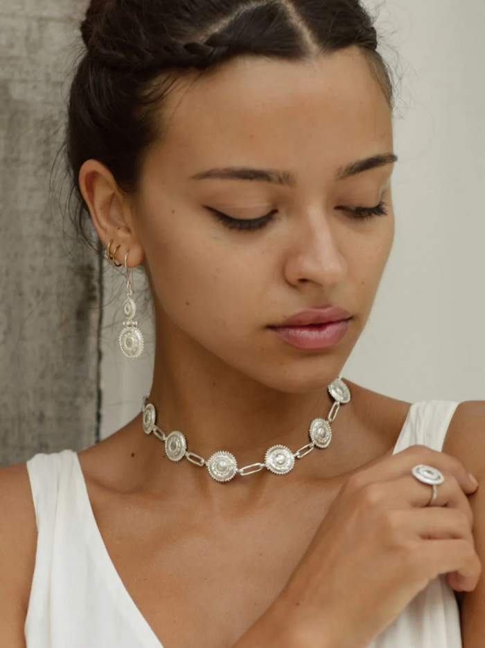 Woman wearing a silver necklace and earrings with a neutral background