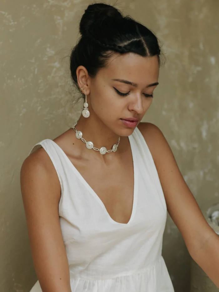 Woman wearing a white sleeveless top and pearl necklace against a neutral background