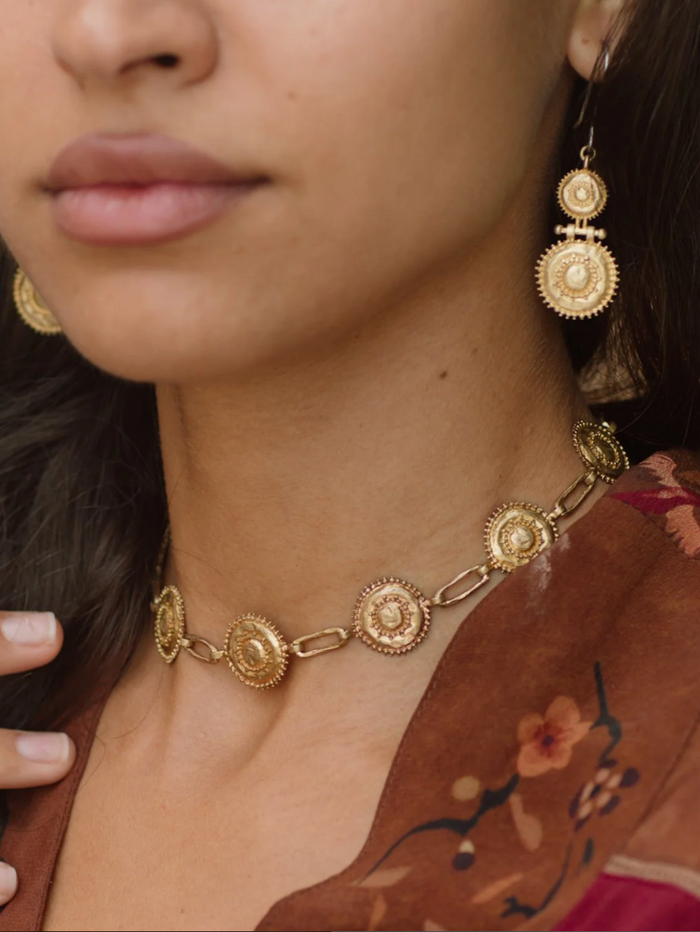 Close-up of a person wearing gold jewelry including earrings and a necklace.