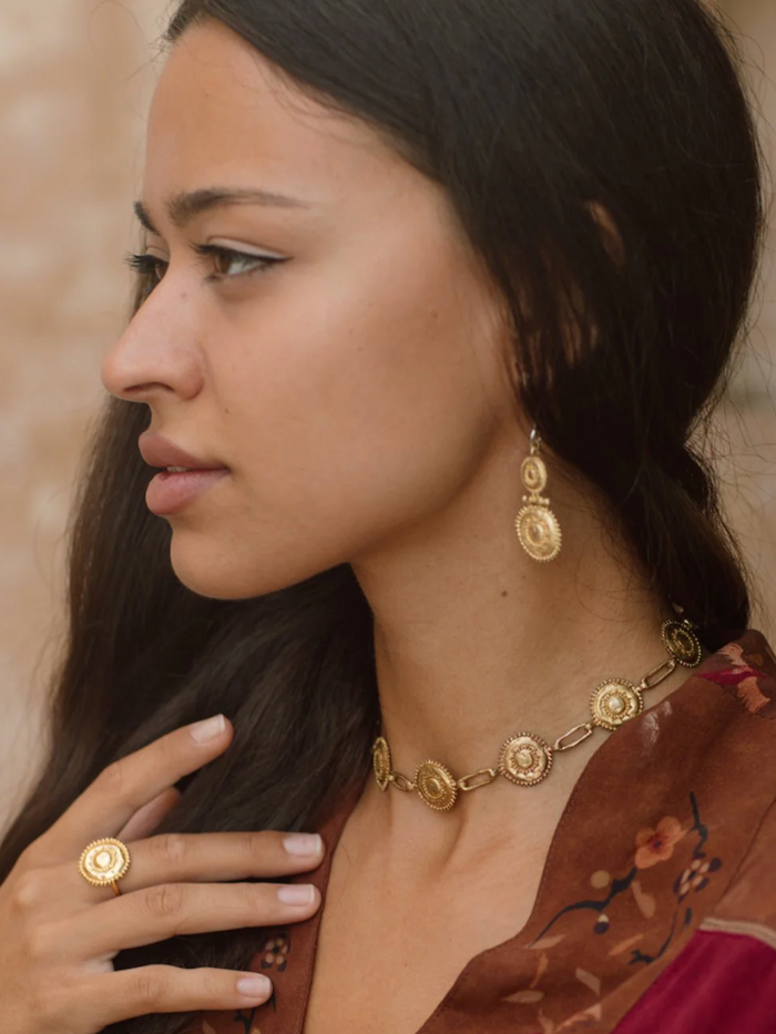 Woman wearing gold jewelry including a necklace, earrings, and ring.