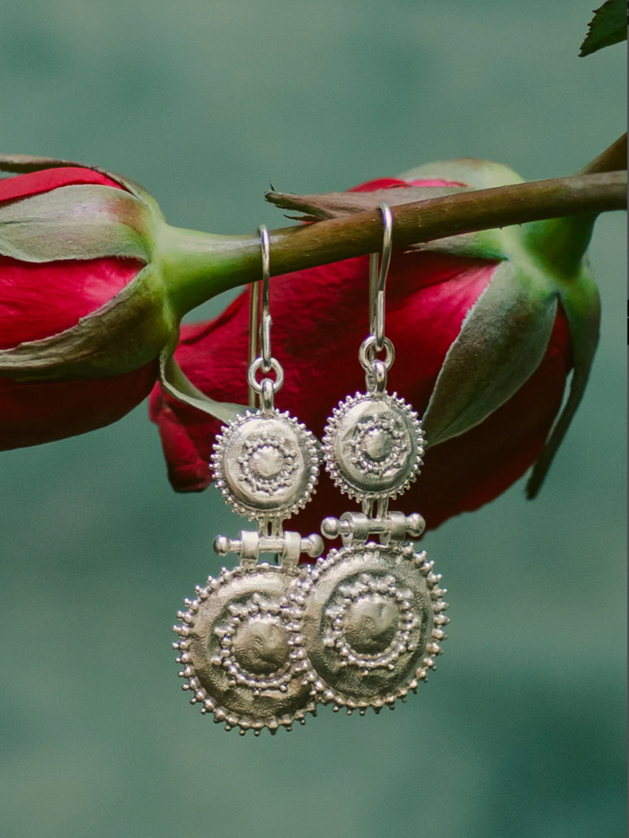 Silver earrings hanging from a red flower bud on a blurred green background