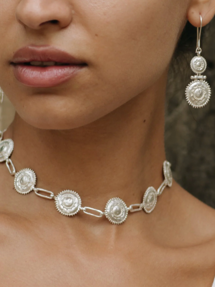 Close-up of a person wearing a silver necklace and earrings.