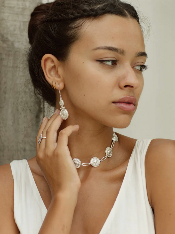 Woman wearing a necklace and earrings with a neutral background