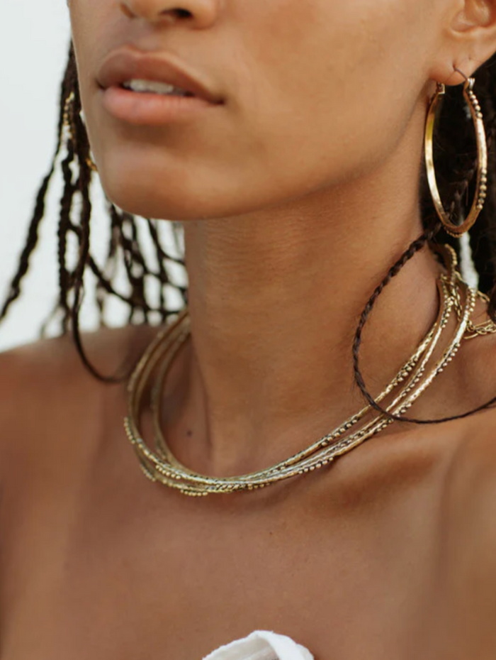 Close-up of a person wearing gold hoop earrings and necklaces.