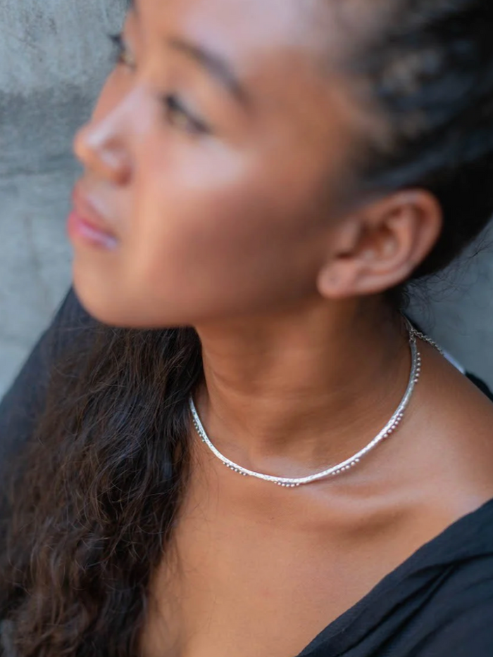 Close-up of a person wearing a silver necklace against a neutral background