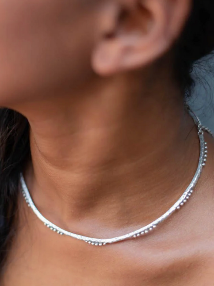 Close-up of a person wearing a silver necklace with a blurred background