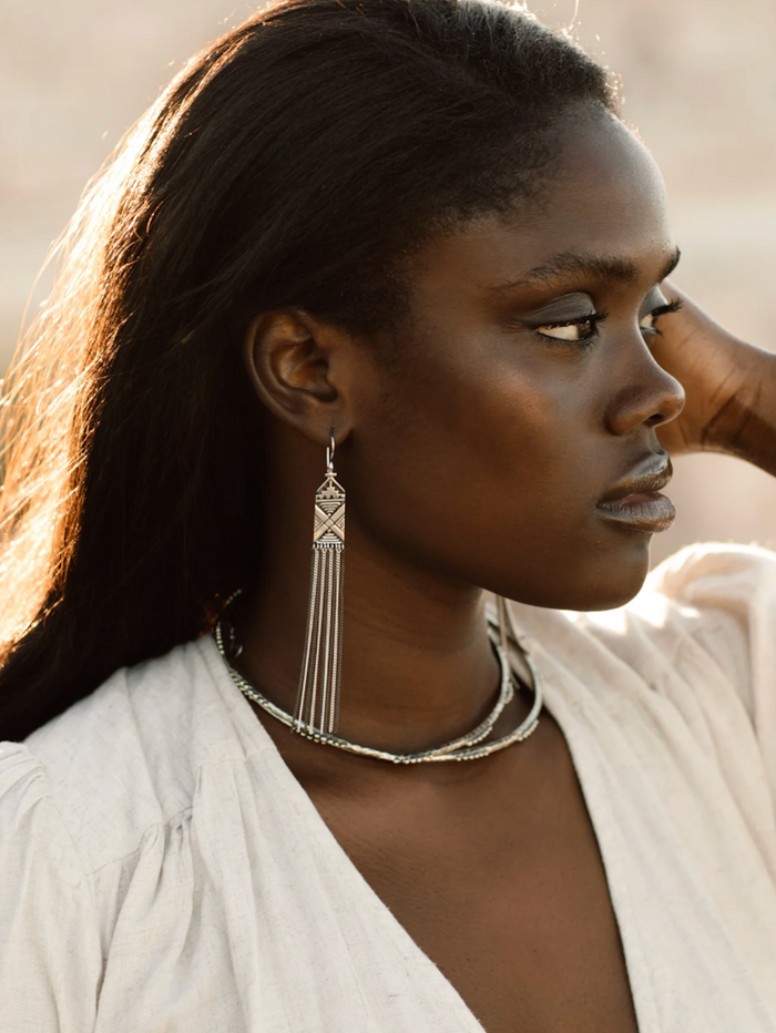 Woman wearing a silver earring and necklace against a neutral background