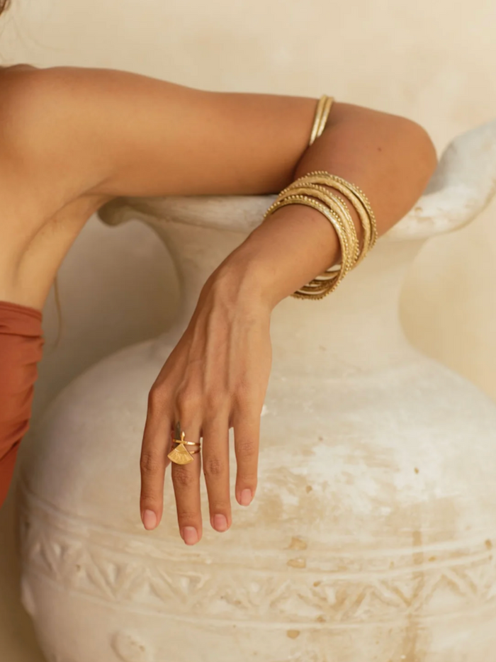 Hand wearing a gold ring and bracelet on a textured surface
