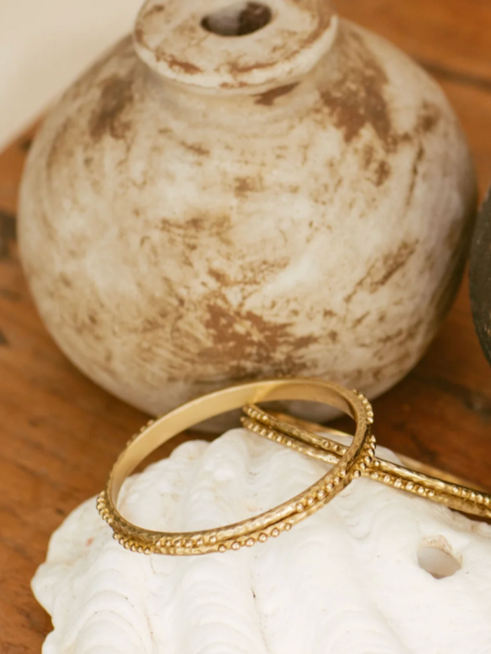 Brass bangles on a white seashell with a textured beige vase in the background
