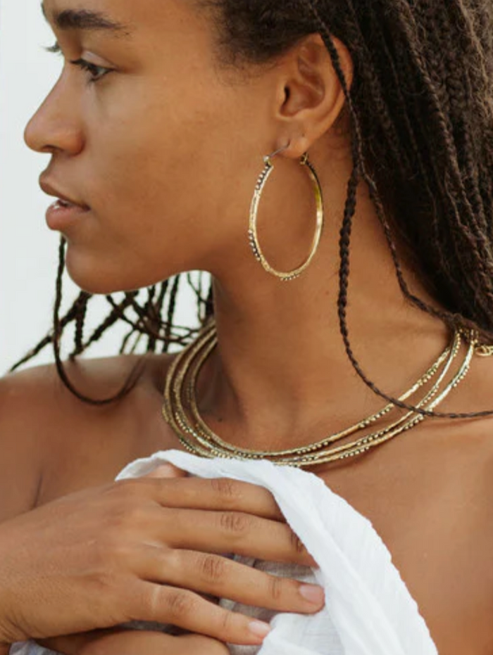 Woman wearing gold hoop earrings and necklaces with a white towel over her shoulder.