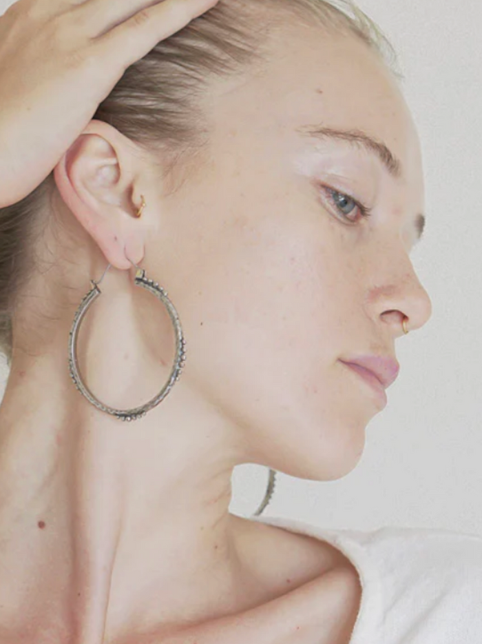 Close-up of a person wearing large hoop earrings with a neutral background