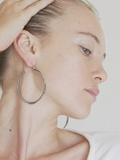 Close-up of a person wearing large hoop earrings with a neutral background