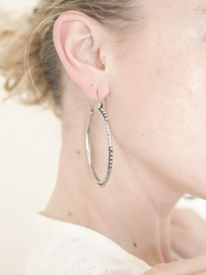 Close-up of an ear wearing a silver hoop earring with a blurred background