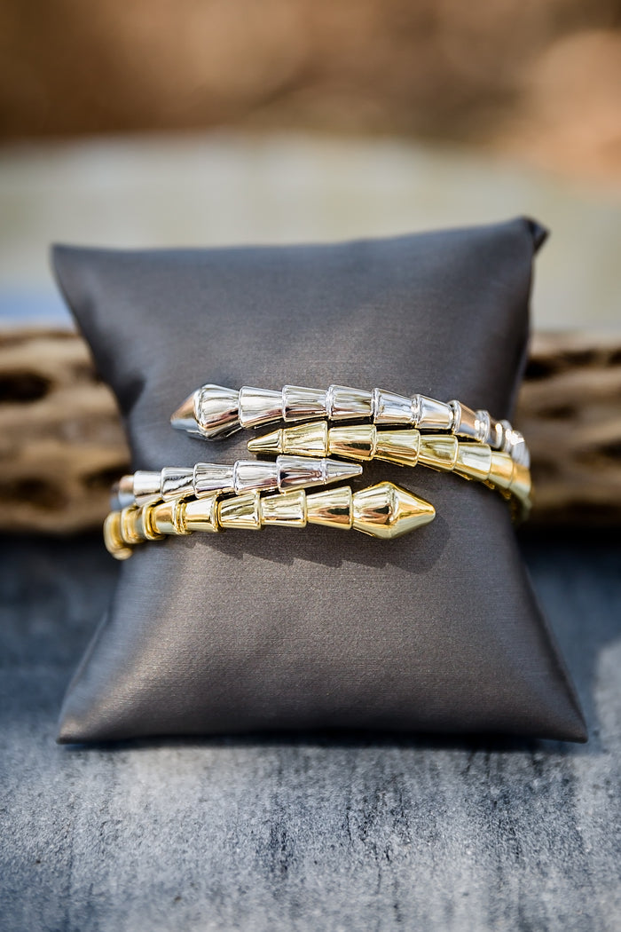 Stacked Night Coil bangles on display pillow showing layered styling with textured coil design and gold finish