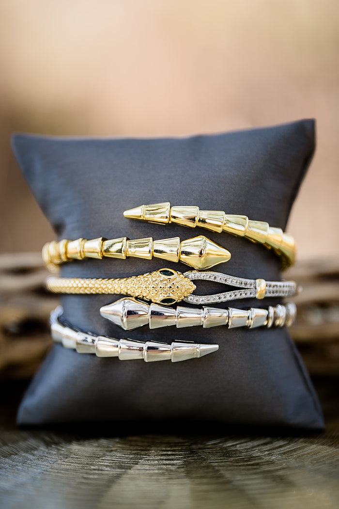 Night Coil gold bangles stacked together on display pillow featuring coil texture and modern stackable design
